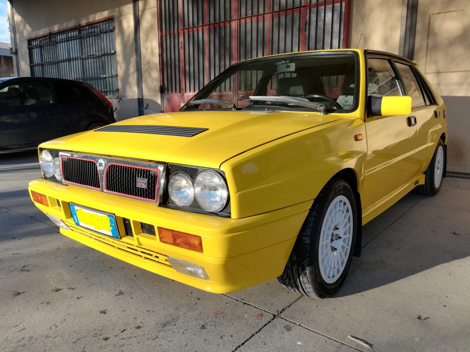 Una Lancia Delta Integrale gialla appena riverniciata davanti all'officina